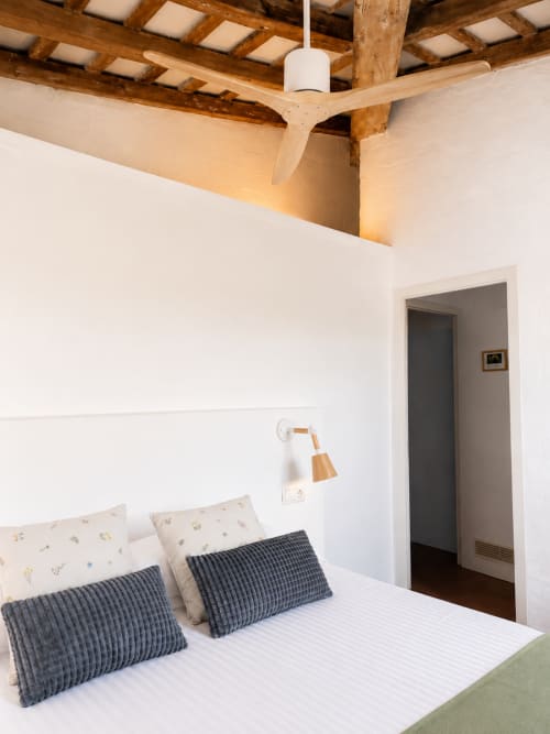 Habitació moderna al Mas Ribas Hotel de Palamós amb bigues de fusta vistes, parets blanques, coixins blaus i ventilador de sostre