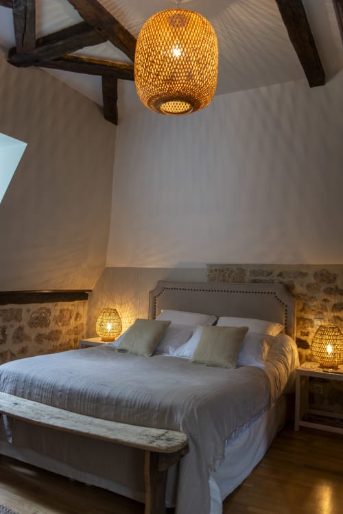 Chambre élégante à La Demeure du Comte avec suspension dorée, plafond à poutres et lampes de chevet vue jardin