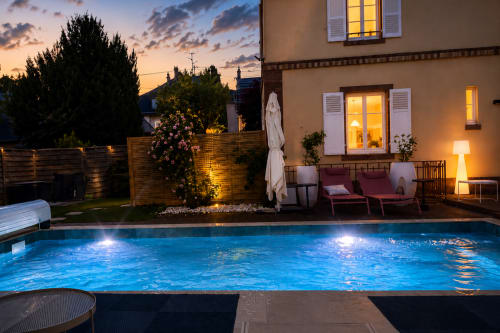 Piscine de la Villa Avril & Spa au crépuscule avec eau illuminée, chaises longues et maison moderne à Sélestat