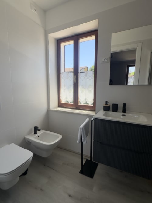 Moderno bagno presso Casale Rusignûl B&B con WC, bidet, lavabo, mobile vanity, specchio e finestra con vista su Cassegliano