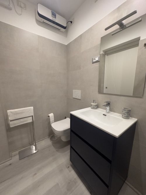 Bagno moderno presso il Casale Rusignûl B&B con vanità nera, lavandino bianco, specchio, scaldasalviette e piastrelle beige