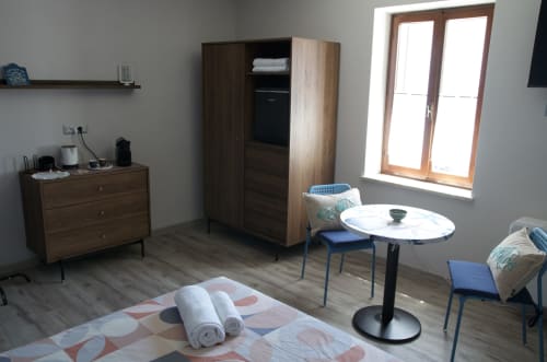 Camera moderna del B&B Casale Rusignûl con mobili in legno, tavolo rotondo e asciugamani arrotolati su tappeto fantasia
