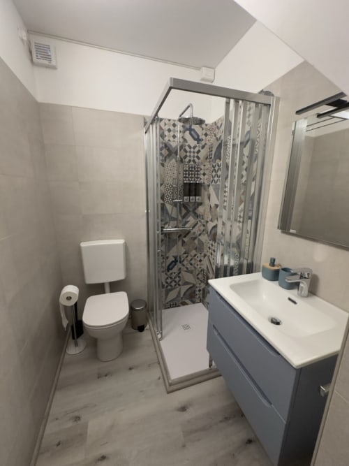 Bagno moderno presso il Casale Rusignûl B&B a Basegliano con doccia, mobile lavabo bianco, WC e pareti con piastrelle decorate