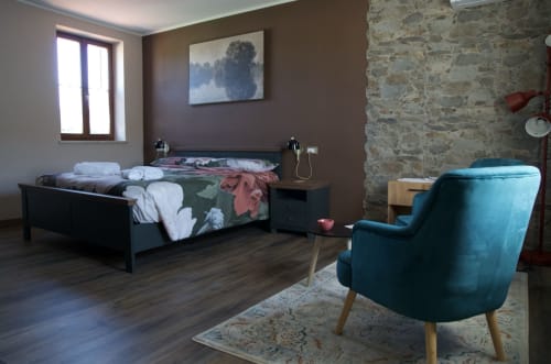 Accogliente camera da letto al Casale Rusignûl B&B di Cassegliano con muri in pietra, letto scuro, sedia turchese e pavimento in legno rustico