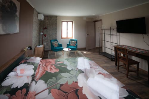 Spaziosa camera da letto al Casale Rusignûl B&B con biancheria floreale, sedie turchesi, TV e parete in pietra