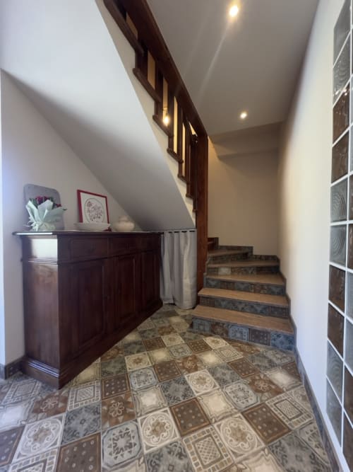 Elegante corridoio con scale presso Casale Rusignûl B&B con pavimento in piastrelle decorate, mobili in legno scuro e illuminazione incassata.