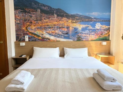 Habitación deluxe en Hostal Zaragoza Centro con cama king-size, almohadas blancas y gran mural de la costa de Mónaco