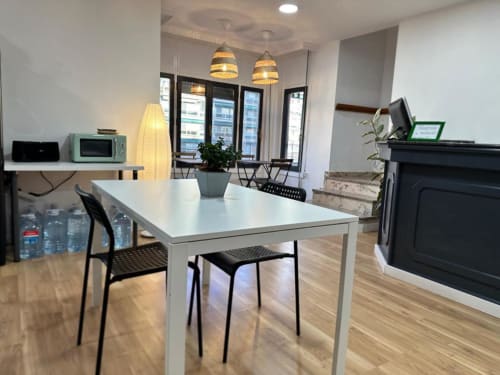 Área común moderna en Hostal Zaragoza Centro con mesa blanca, luces colgantes, chimenea y electrodomésticos de cocina