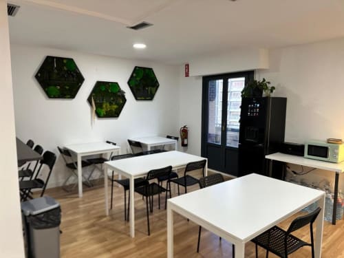 Área común moderna de Hostal Zaragoza Centro con mesas blancas, sillas negras y arte de pared vegetal
