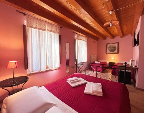 Camera da letto rosa brillante a Corte Pellegrini B&B a Verona con letto rosso, travi in legno e testata ornamentale