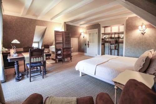 Chambre spacieuse à La Maison Oubliée avec poutres blanches, papier peint marron, lit et mobilier vintage à Goetzenbruck.