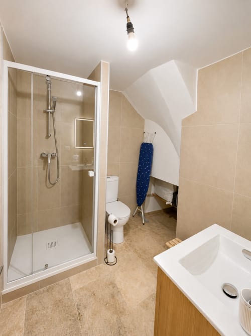 Salle de bain moderne avec douche à l'italienne, toilettes, lavabo et planche à repasser dans l'appartement By Elodie, Hyères