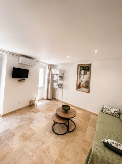 Modern apartment living room in Hyères with TV, wooden nesting tables, green sofa, and natural light