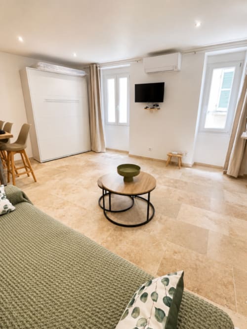 Salon moderne à Hyères avec sol beige, canapé, table basse ronde, téléviseur écran plat et cuisine