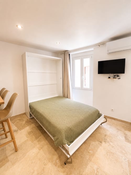 Studio moderne à Hyères avec lit escamotable blanc, TV murale, mobilier en bois et carrelage