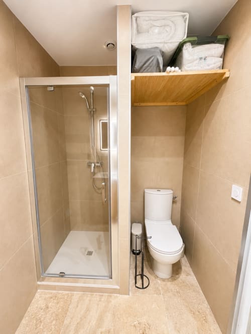 Salle de bain moderne avec douche, toilettes et étagères de rangement en bois dans l'appartement By Elodie, Hyères