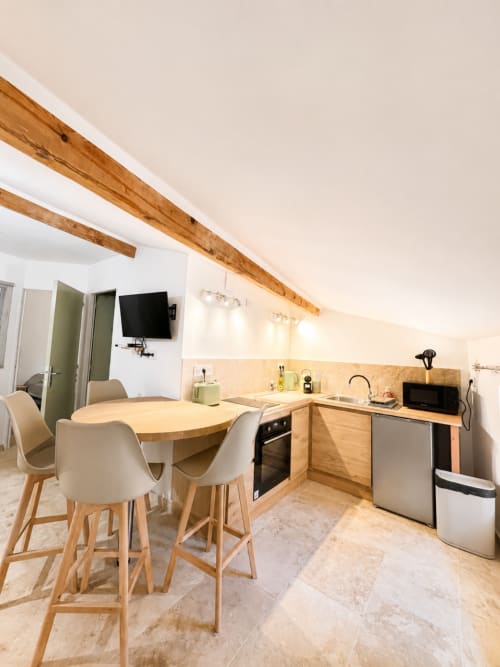 Modern kitchen-dining area at By Elodie apartment in Hyères with wooden beams, dining table, and equipped kitchenette