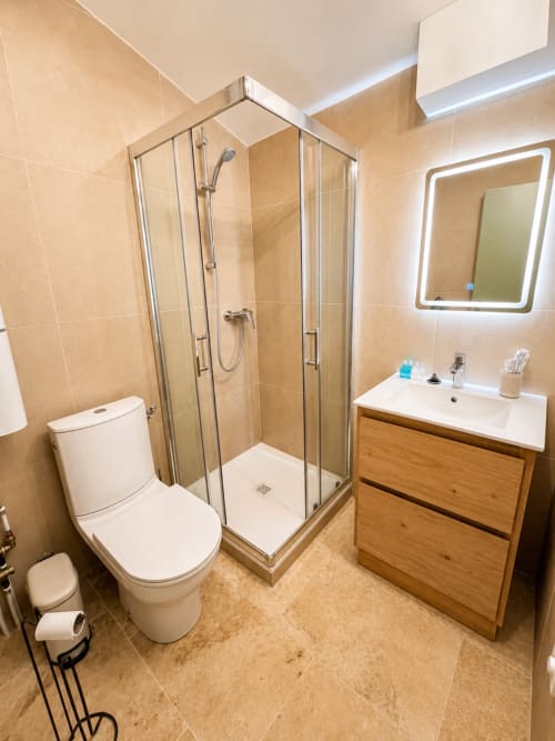 Salle de bain moderne dans l'appartement By Elodie à Hyères avec douche, toilettes, meuble vasque en bois et miroir LED