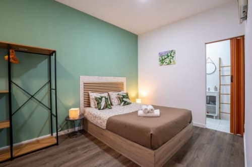 Quarto de casal moderno em Madeirarooms Funchal com parede de destaque verde menta, cama de madeira e móveis contemporâneos