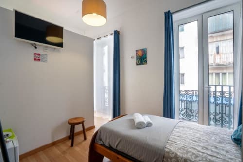 Quarto individual com varanda em Madeirarooms Funchal, com cama, TV e portas com vista para a cidade