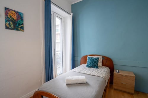 Quarto único com cama de madeira, parede de destaque em azul-petróleo, porta para varanda e vista da cidade no hotel Madeirarooms em Funchal