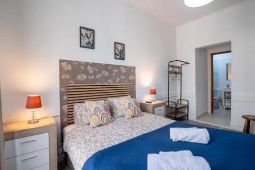 Quarto duplo moderno em Madeirarooms Funchal com acentos azuis, cabeceira listrada, luminárias e casa de banho privativa
