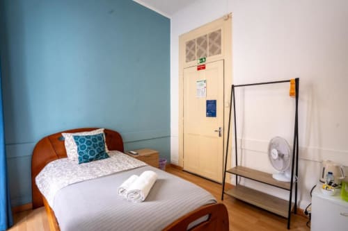 Quarto individual do hotel Madeirarooms em Funchal com cama de madeira, parede azul acentuada, ventilador e guarda-roupa branco