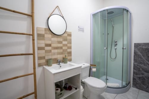 Banheiro moderno do hotel Madeirarooms com lavatório, WC, box para duche, espelho redondo e azulejo bege na parede