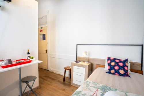 Quarto individual na Madeirarooms em Funchal com cama, secretária, piso em madeira e vista para a cidade do terraço