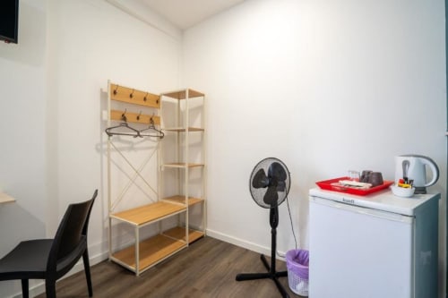 Canto moderno de quarto em hotel Madeirarooms Funchal com prateleira de madeira, ganchos na parede, ventilador preto, armário branco e