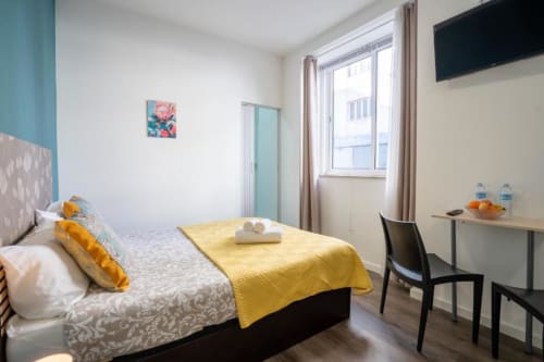 Quarto duplo luminoso no hotel Madeirarooms em Funchal com vista da cidade, decoração com detalhes amarelos, TV e mobiliário moderno