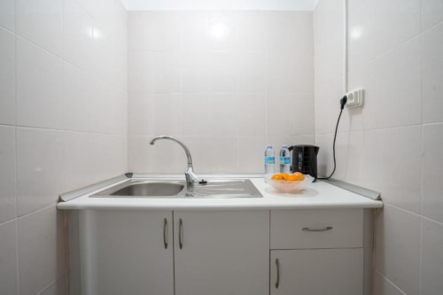 Kitchenette moderna no quarto do hotel Madeirarooms com azulejos brancos, pia, fogão e bancada equipada