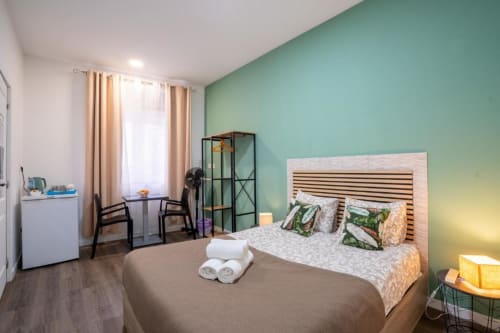 Quarto duplo moderno da Madeirarooms Funchal com parede de destaque verde menta, cama de madeira, escrivaninha e janelas com vista para a cidade
