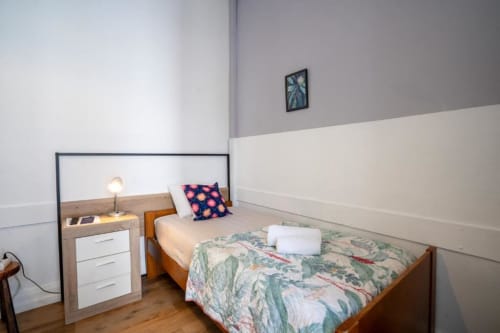 Quarto individual da Madeirarooms Funchal com cama de madeira, luminária de cabeceira, roupa de cama estampada e paredes em tons duplos
