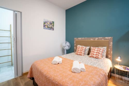Quarto moderno da Madeirarooms em Funchal com parede de destaque em azul-petróleo, cama de madeira, roupa de cama coral e serviço de toalhas