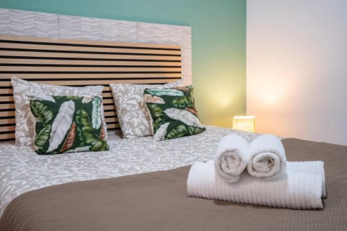 Quarto moderno do Madeirarooms em Funchal com cabeceira listrada, almofadas tropicais, toalhas enroladas e iluminação ambiente