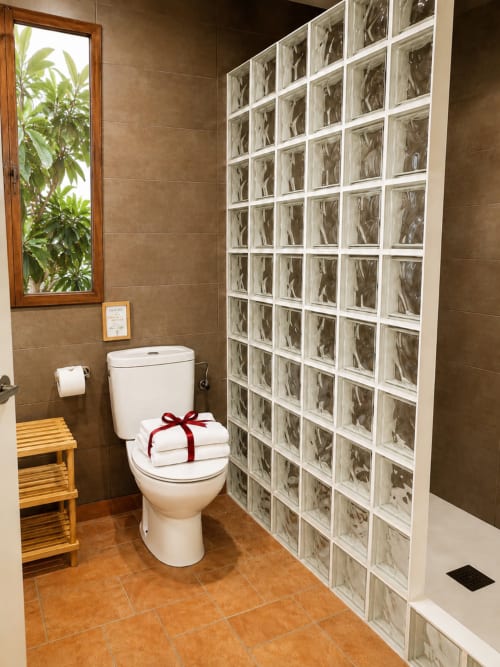 Modern bathroom at Mas Ribas Hotel with glass block shower, white toilet, terracotta tiles, and garden view window in Palamós