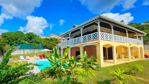 Villa coloniale jaune avec piscine, jardins tropicaux luxuriants et balustrade blanche surplombant la piscine turquoise
