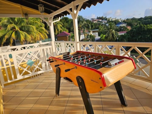 Table de baby-foot orange sur la terrasse de la Villa Calebassier avec vue tropicale sur les palmiers et le paysage caribéen
