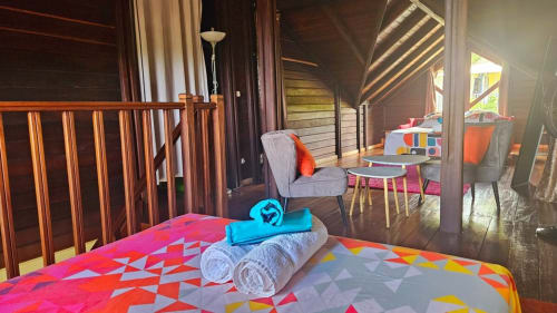 Chambre colorée à la Villa Calebassier avec literie géométrique, serviettes roulées, fauteuil et terrasse ouverte sur piscine