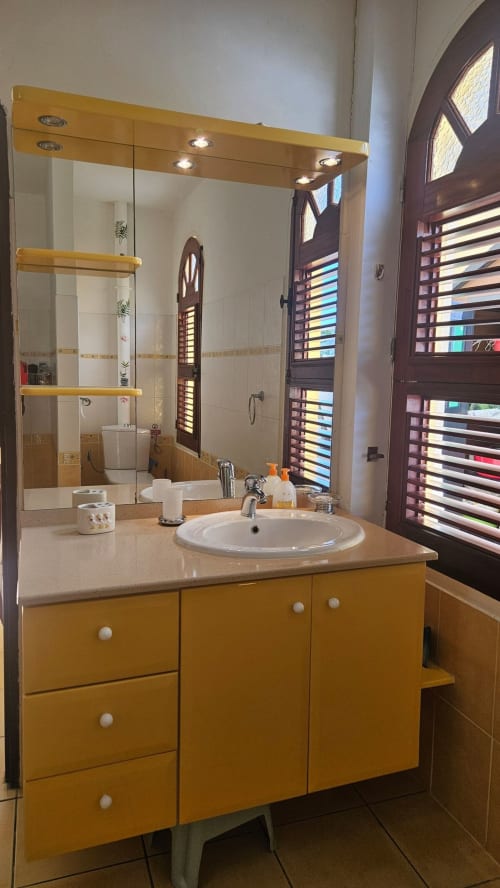 Salle de bain contemporaine avec meuble-lavabo jaune doré, lavabo rond blanc, grand miroir éclairé et porte en bois foncé dans une villa