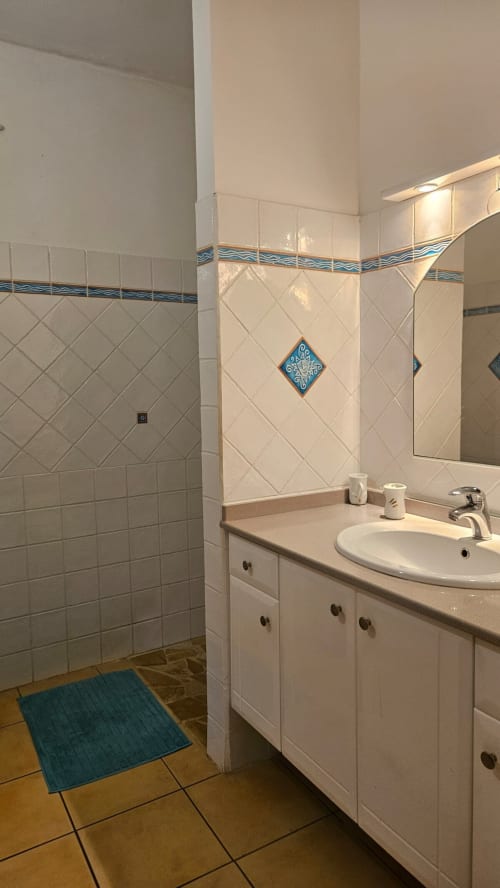 Salle de bain moderne avec carrelage blanc, touches décoratives bleues, lavabo rond, rangements et miroir à la Villa Calebassier