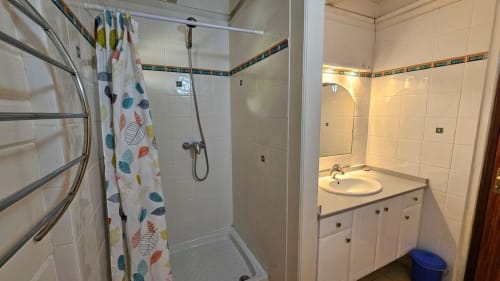 Salle de bains moderne aux murs carrelés blanc, douche à l'italienne avec rideau à motifs de feuilles, et lavabo vanité à la Villa Calebassier