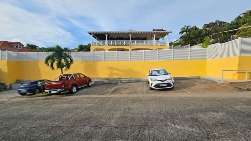 Parking de Villa La Suite Viva Vero avec murs jaunes, palmier, clôture blanche et villa coloniale colorée