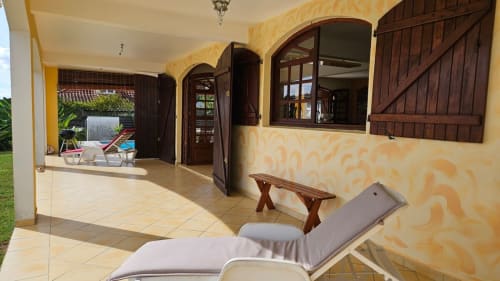 Terrasse couverte avec chaise longue, banc en bois et portes cintrées, vue piscine à Villa La Suite Viva Vero