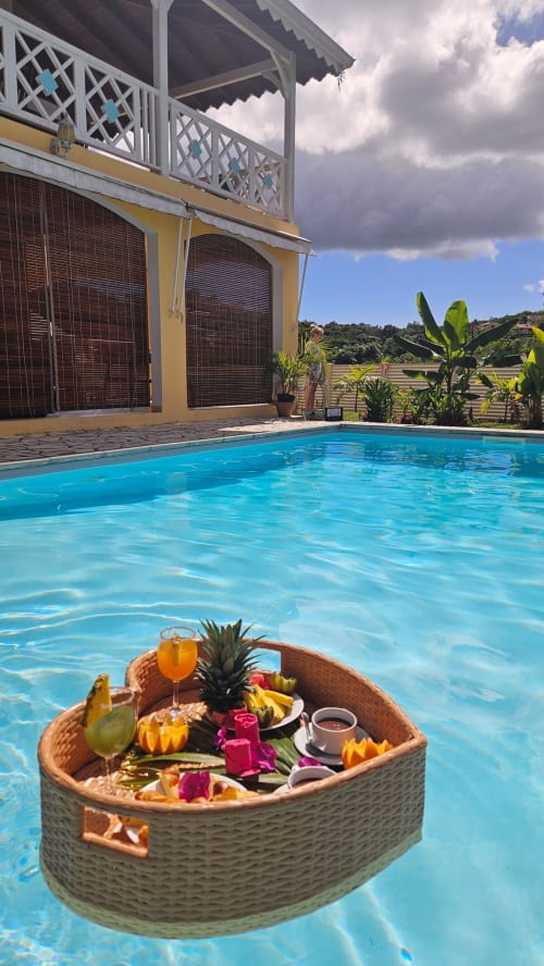 Petit-déjeuner de luxe sur matelas flottant dans la piscine turquoise de Villa La Suite Viva Vero, avec villa jaune et jardins tropicaux