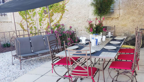 Terrasse extérieure avec chaises rouges et roses, tables dressées, fleurs et mur en pierre aux Villas Lux Tropical à Béziers