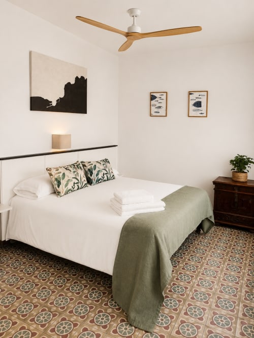 Habitació moderna de l'hotel Mas Ribas a Palamós amb llit blanc, ventilador de sostre de fusta i paviment de rajoles amb motius
