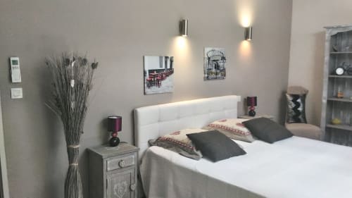 Chambre moderne avec tête de lit blanche capitonnée, coussins foncés, art mural contemporain, lampes de chevet et décoration sèche