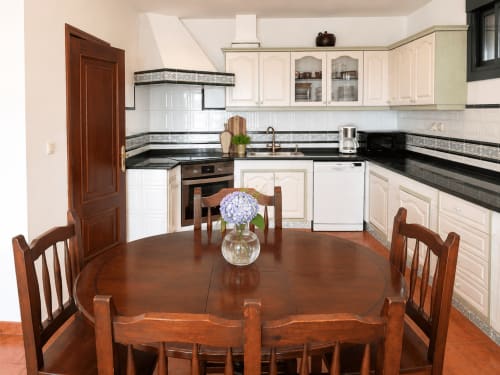 Elegante comedor de la casita Vila Santa Rita en Oia, con mesa de madera, muebles de cocina blancos y granito negro